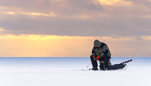 Solitary man ice fishing on a lake at sunset.
