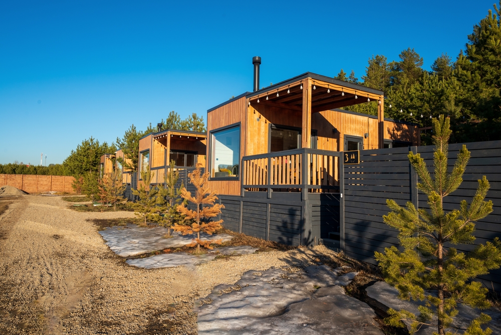 Small, wooden cottages or bunkies surrounded by trees and a dark grey fence.