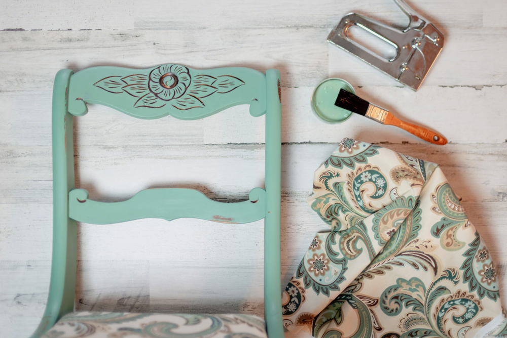 Teal-coloured vintage chair next to patterned fabric and a staple gun.