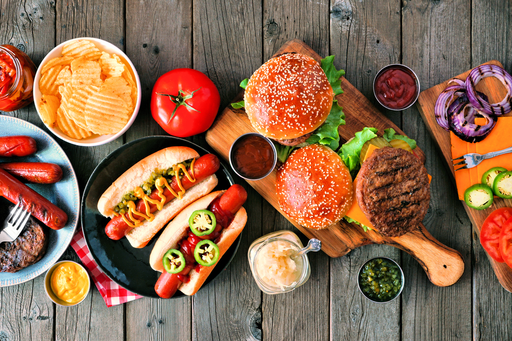 Overhead view of hamburgers and hotdogs against a dark wood background.