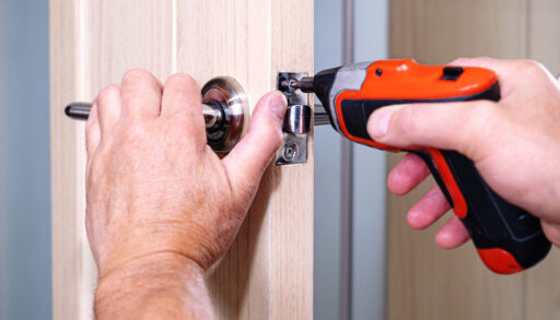 Man using a red electric screwdriver to attach a screw to a door.