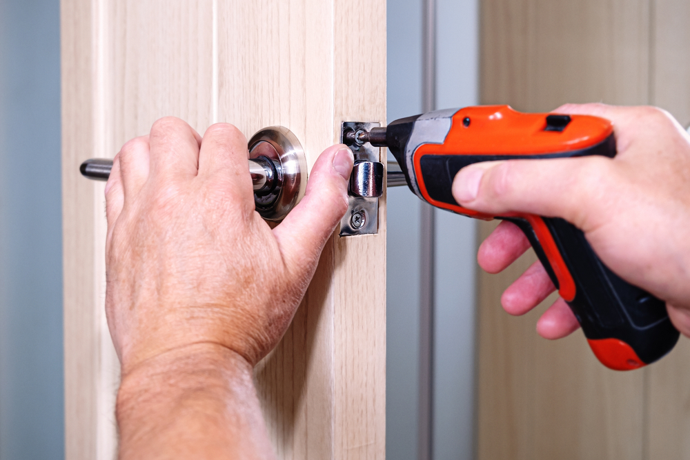 Man using a red electric screwdriver to attach a screw to a door.