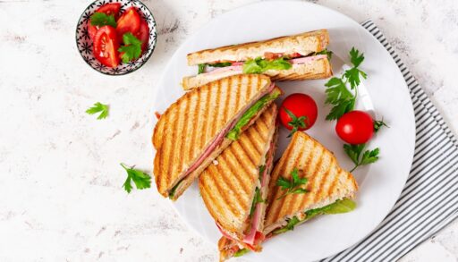 Overhead view of panini sandwiches on a plate next to a bowl of red tomatoes.