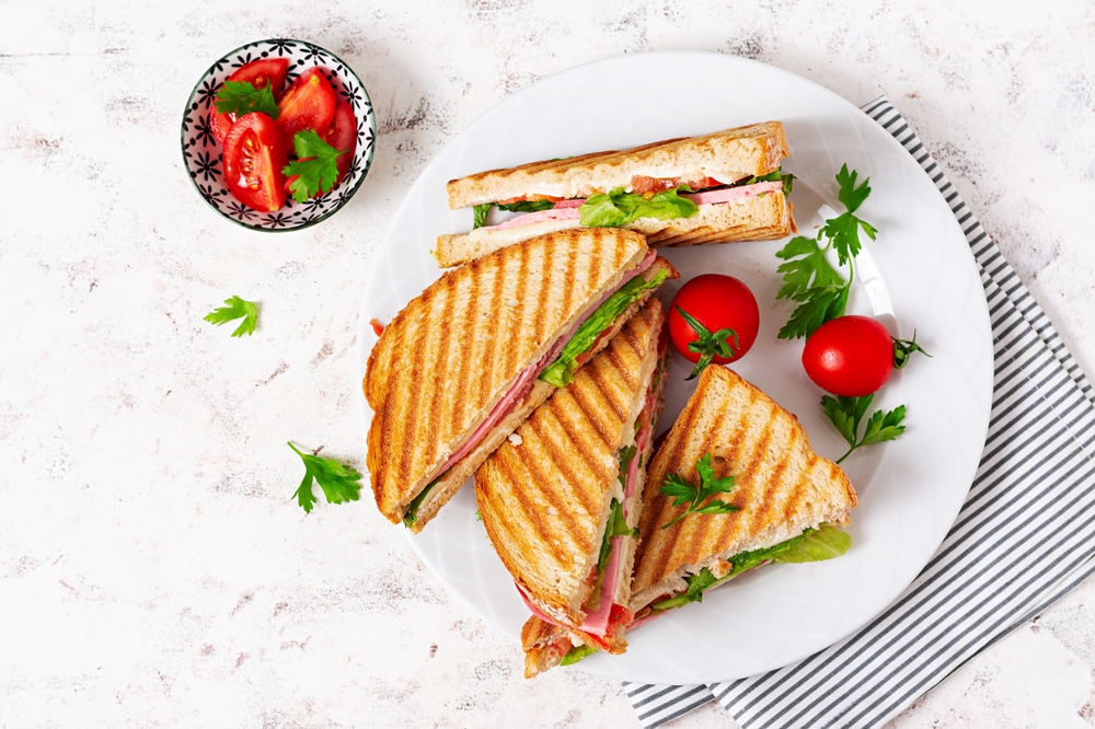 Overhead view of panini sandwiches on a plate next to a bowl of red tomatoes.
