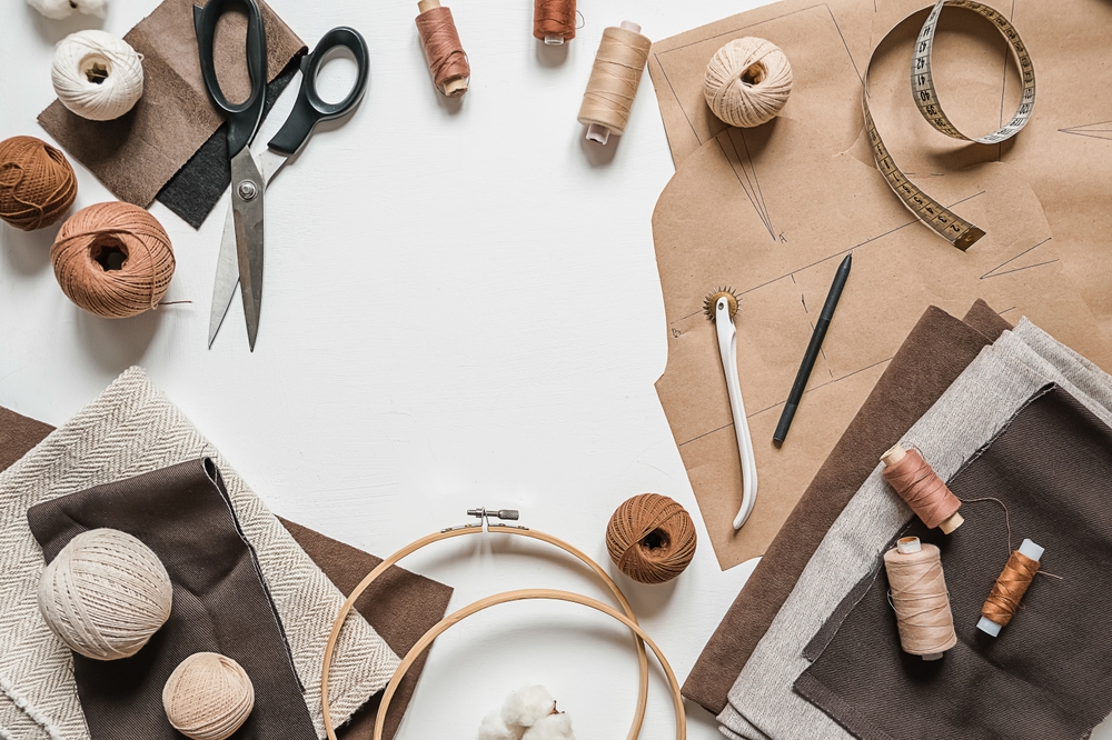 Flat lay of craft materials and recycled paper, with scissors, thread and a tape measure.