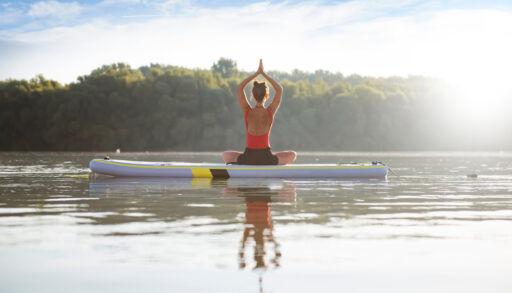 Young woman meditating and doing yoga on a paddleboard on a lake.