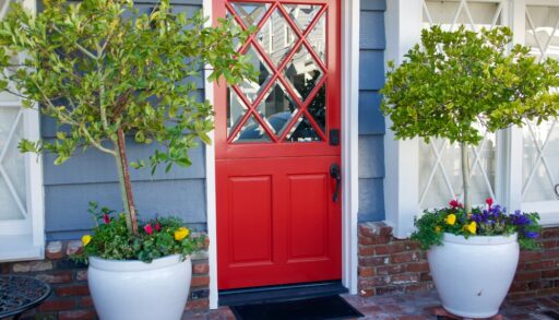 Red front door with two large trees on either side.