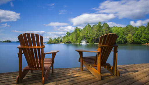 Two Adirondack chairs on a dock looking out over a lake.