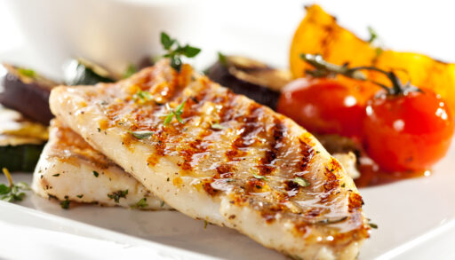 Grilled fish on a plate with red tomatoes and other vegetables.