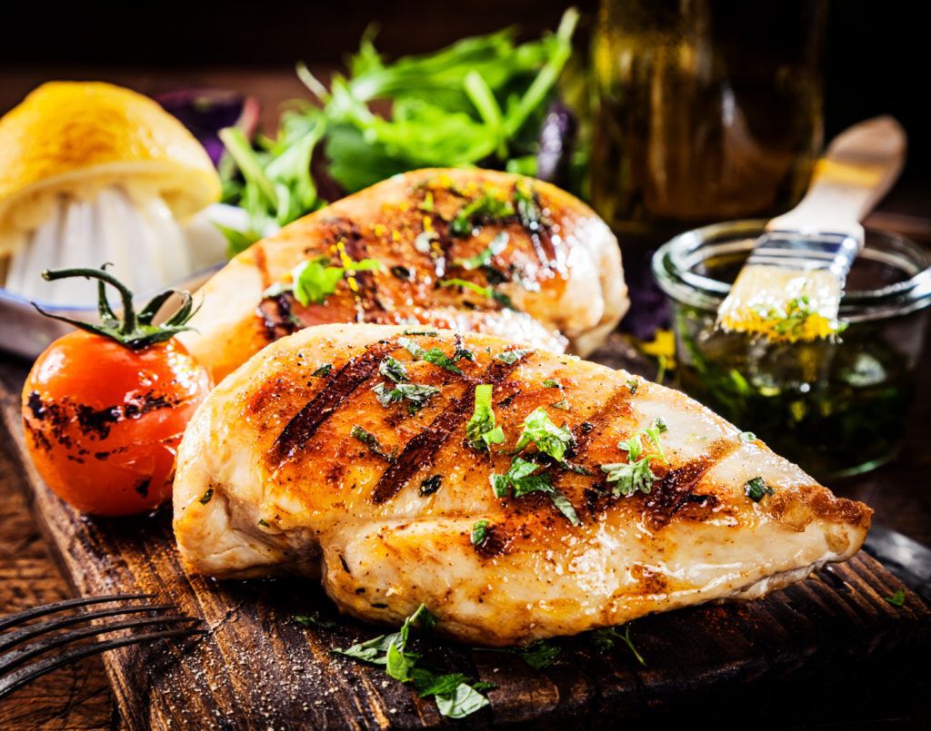 Grilled chicken breasts on a wooden cutting board.
