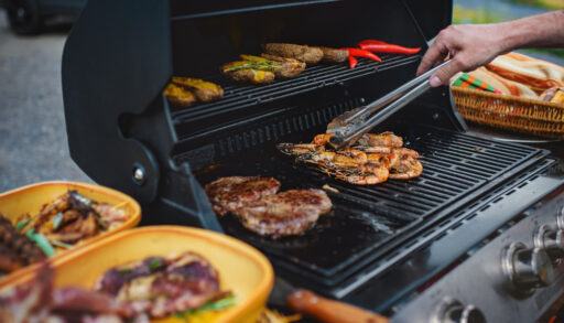 Person using tongs to flip food on a grill.