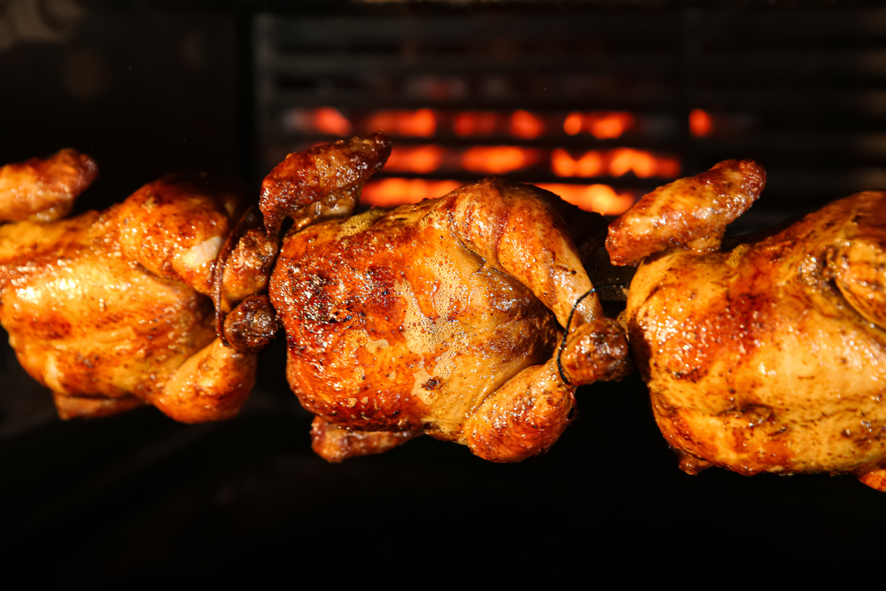 Close-up of three rotisserie chickens on a grill.