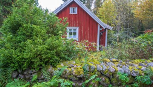 Red cottage surrounded by trees and a garden wall.