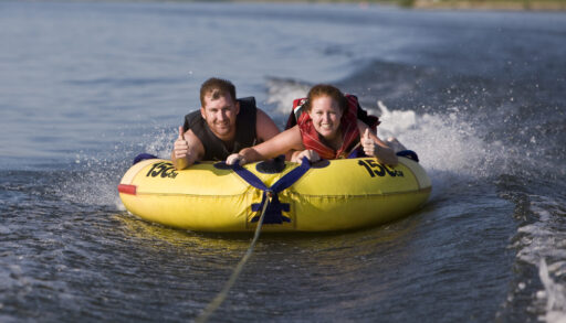 Young man and woman riding a yellow water tube.