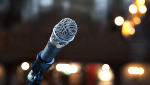 Silver microphone on a stand with a blurred crowd in the background.