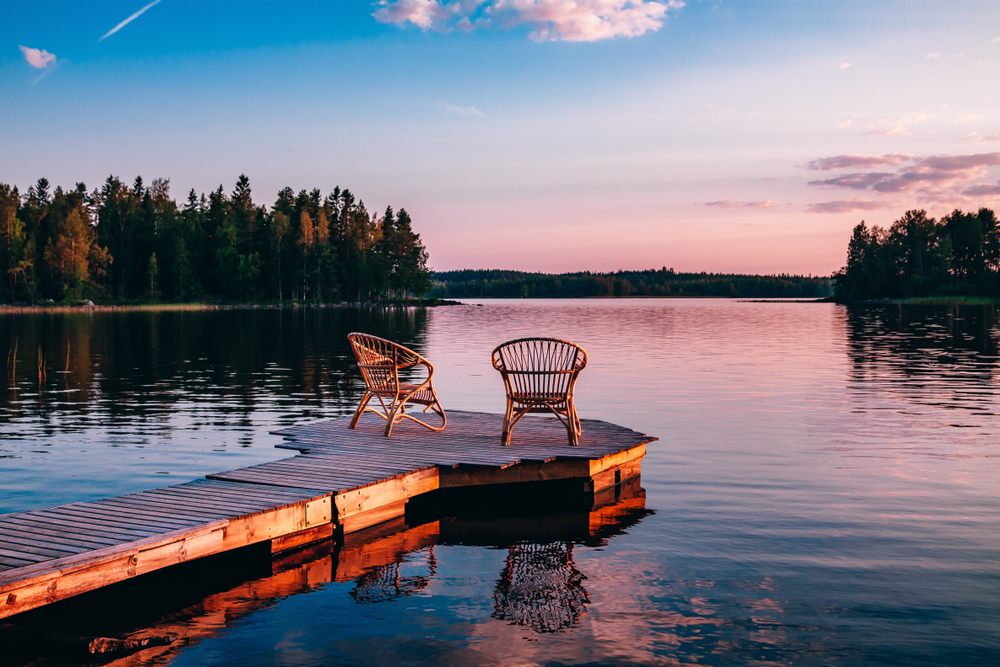 Sunset on a lake with a dock and two chairs.