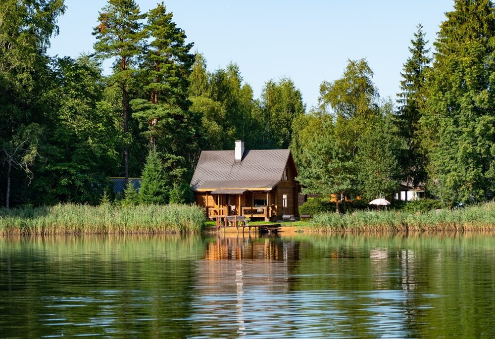 Small, wooden cabin surrounded by trees near a lake.
