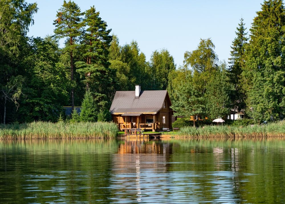 Small, wooden cabin surrounded by trees near a lake.
