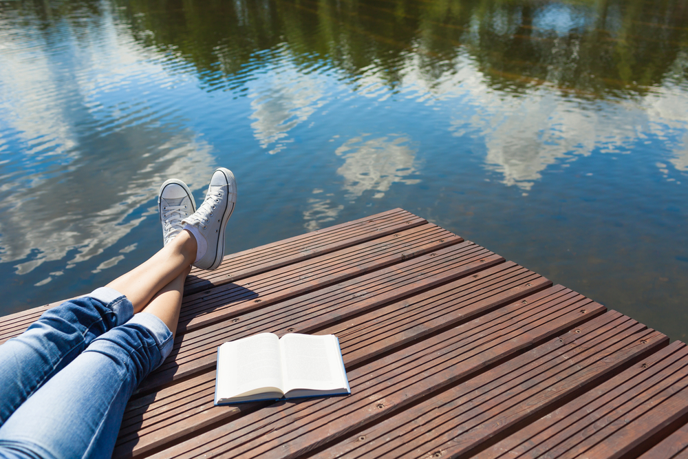 Woman's legs crossed on a dock next to a book.