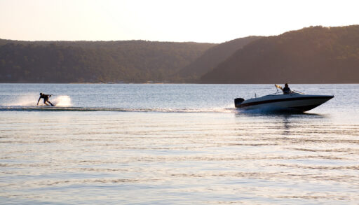 Person waterskiing behind a boat on a lake at sunset.