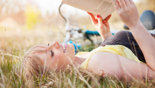 Young girl laying in the grass reading a book.