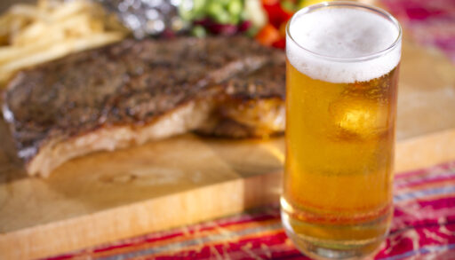 Beer glass in front of a plate with ribs on it.
