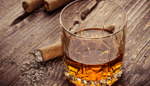 Glass of whiskey next to a cigar on a wooden table.