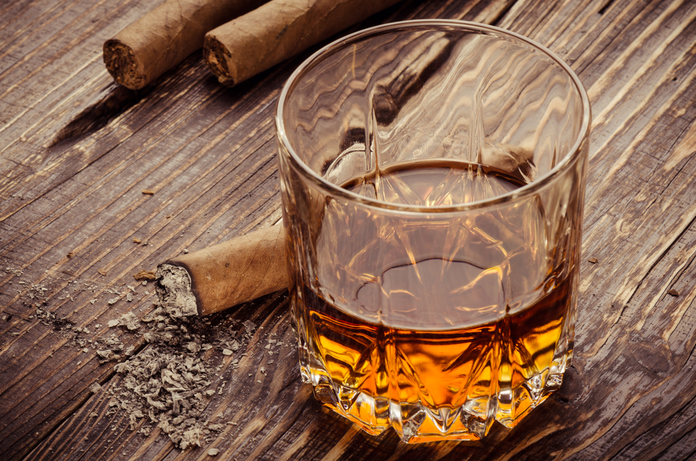 Glass of whiskey next to a cigar on a wooden table.
