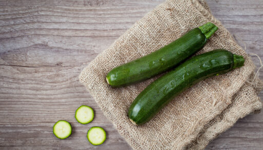 Overhead view of two green zucchini on a piece of burlap next to slices of zucchini.