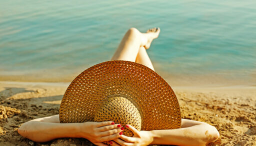 Woman laying on beach wearing a sunhat.
