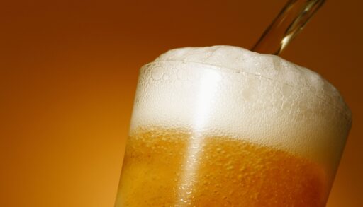Close-up of the top of a beer glass with beer being poured into it.
