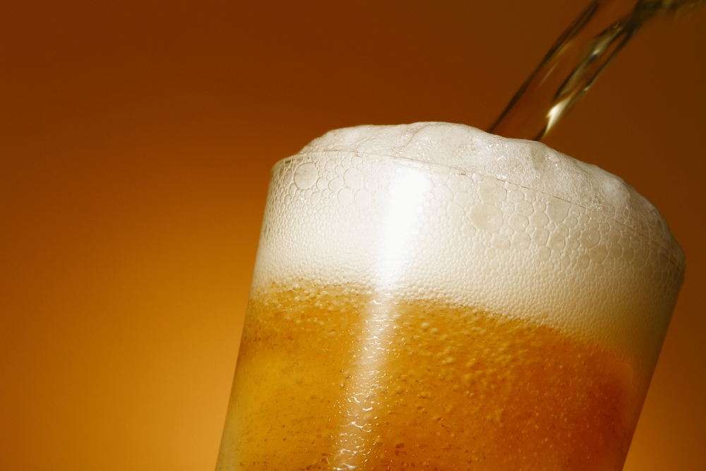 Close-up of the top of a beer glass with beer being poured into it.