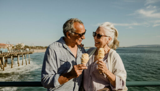 Older man and woman stand on a pier together eating ice cream.