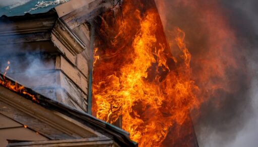 Wooden house with flames coming out of a window.