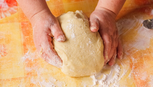 Person with flour-covered hands rolling out a ball of dough.