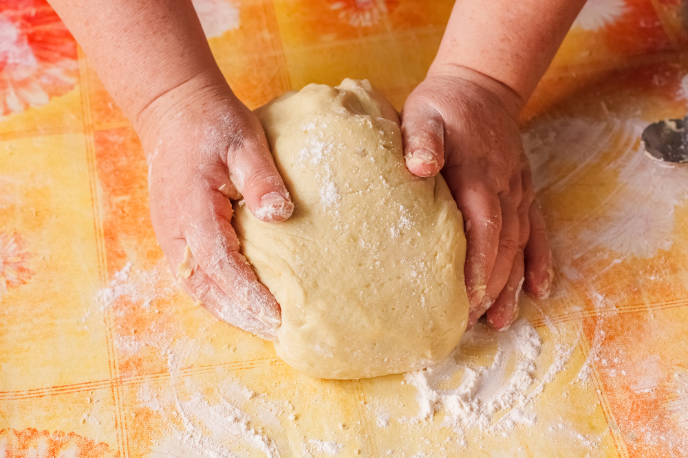 Person with flour-covered hands rolling out a ball of dough.