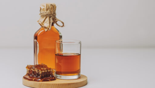 Amber-coloured mead in a glass next to a full glass bottle.