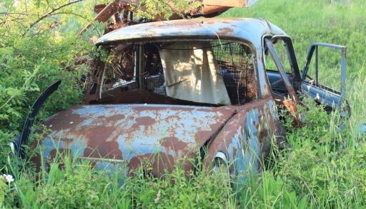 Blue, rusted abandoned car in a field.