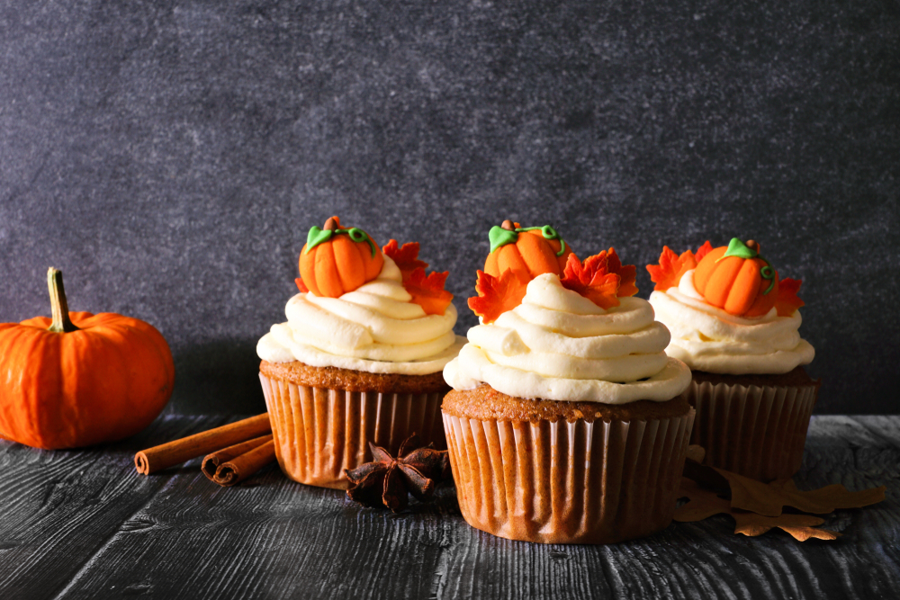 Pumpkin spice cupcakes decorated with white frosting and tiny pumpkins.