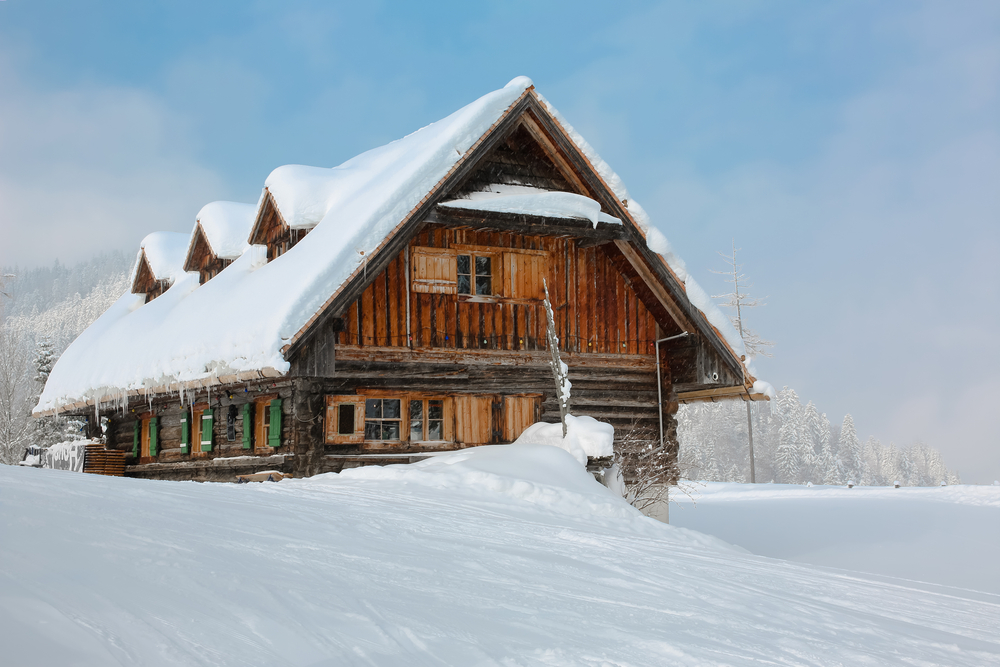 Snow-covered winter cabin in an empty, snowy field.