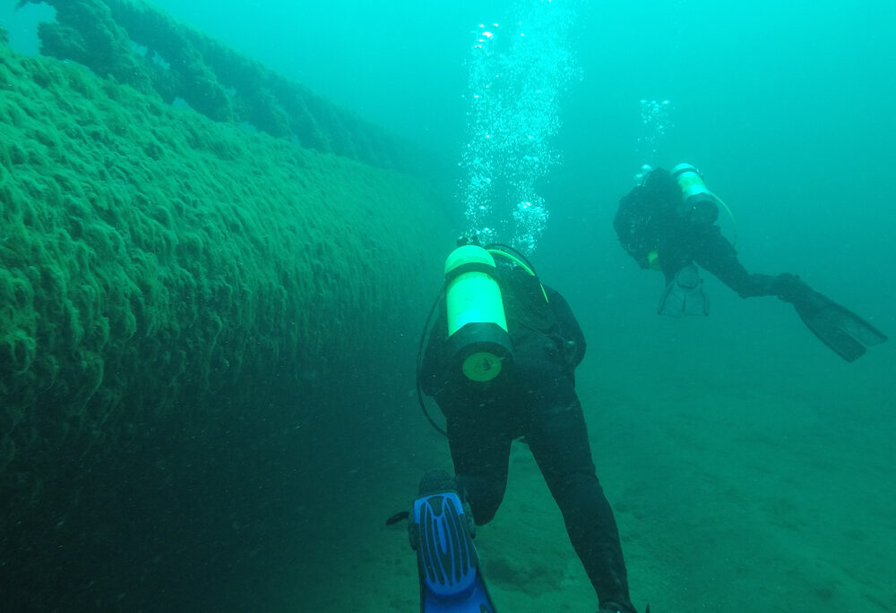 Two scuba divers swim near a shipwreck in the Great Lakes.