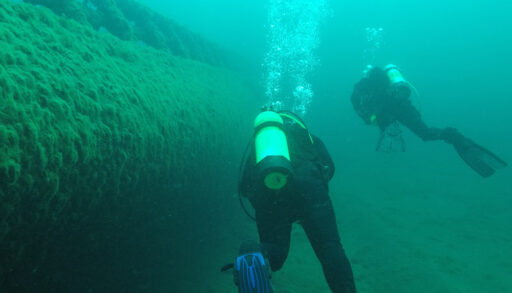 Two scuba divers swim near a shipwreck in the Great Lakes.