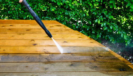 Close-up of a person using a pressure washer to clean a deck.