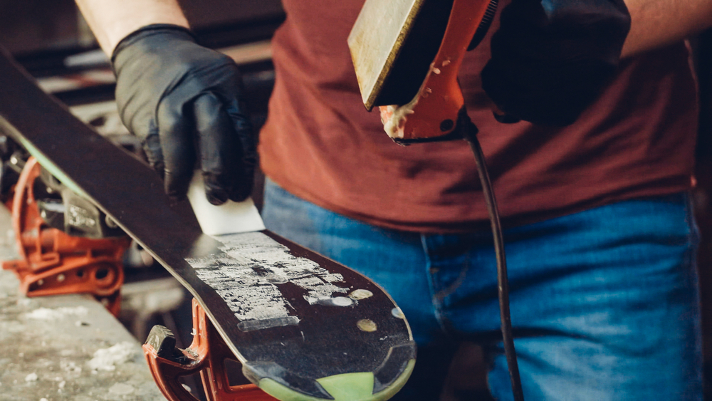 Close-up of a person applying wax to the bottom of a ski.