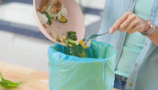 Woman scraping food from a plate into a garbage bin.
