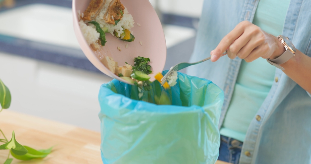 Woman scraping food from a plate into a garbage bin.