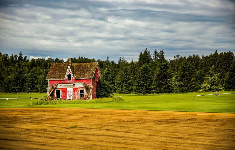 Abandoned red farmhouse in the middle of a field.