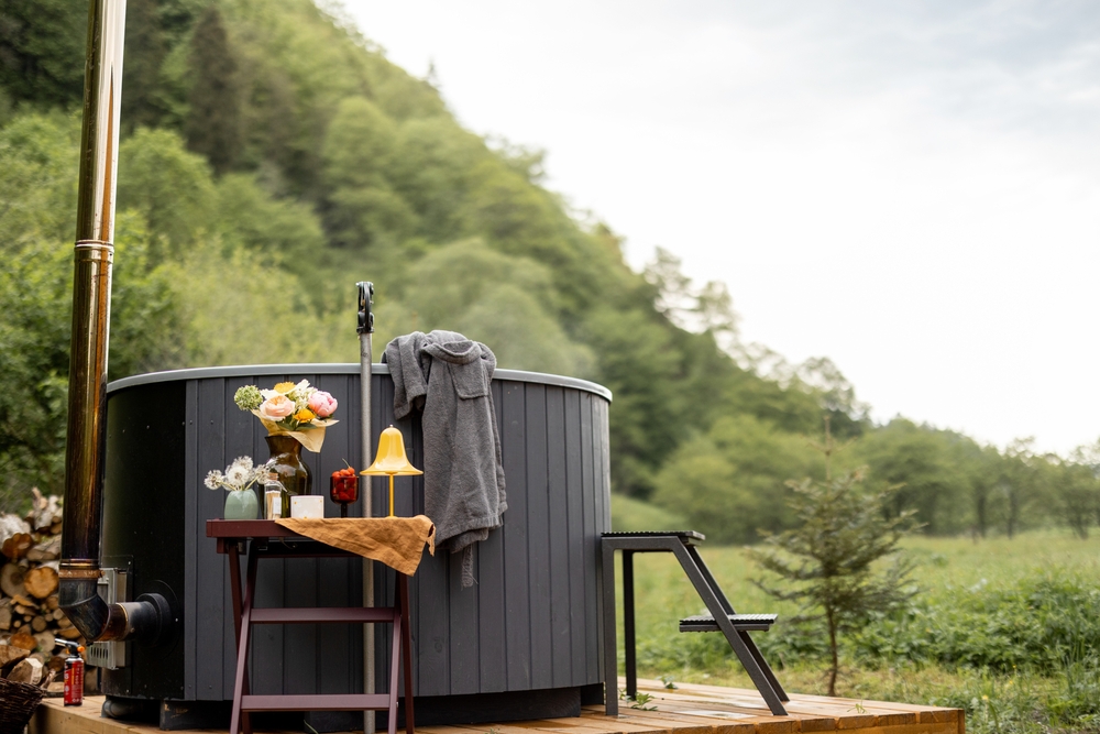 Small, grey hot tub on a wooden deck surrounded by trees.