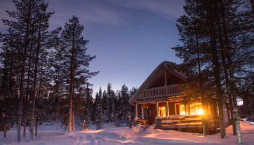 Wooden cabin illuminated at night in a snowy forest.