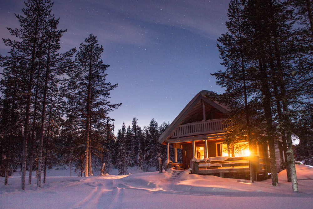Wooden cabin illuminated at night in a snowy forest.